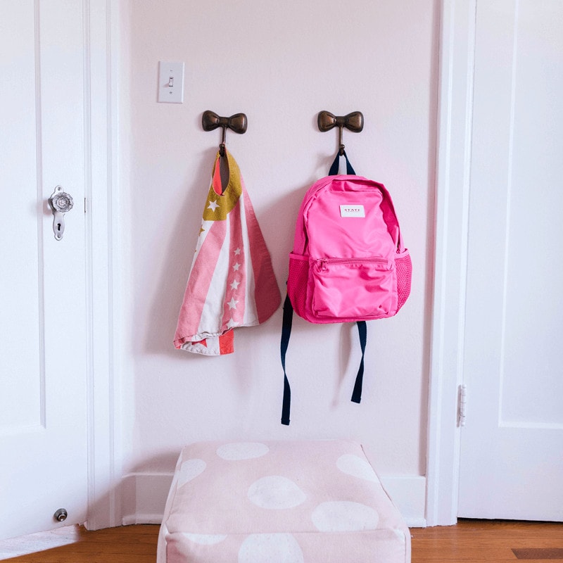two pink bags hanging on hooks in a pale pink bedroom