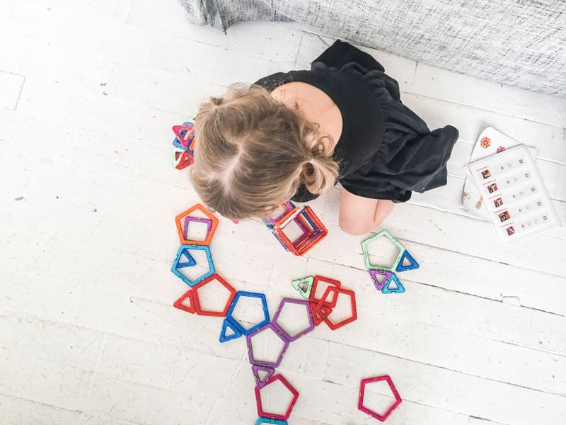 A young girl sitting on a white floor playing with colorful magnetic toys.