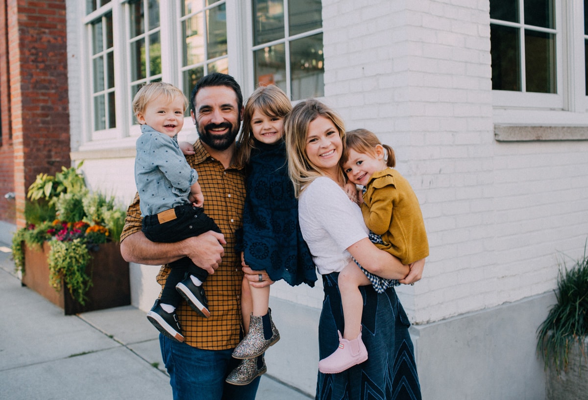 A man and a woman standing with their three children in front of a white building in front of a white building