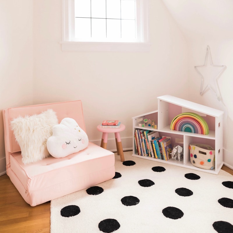A kids' reading space with pink chair, polkadot rug, and bookshelf.