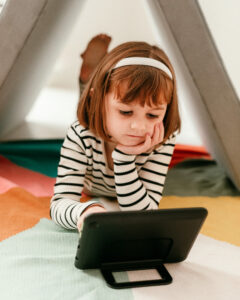 A girl laying on the ground playing with an Amazon Fire Kids Pro Tablet