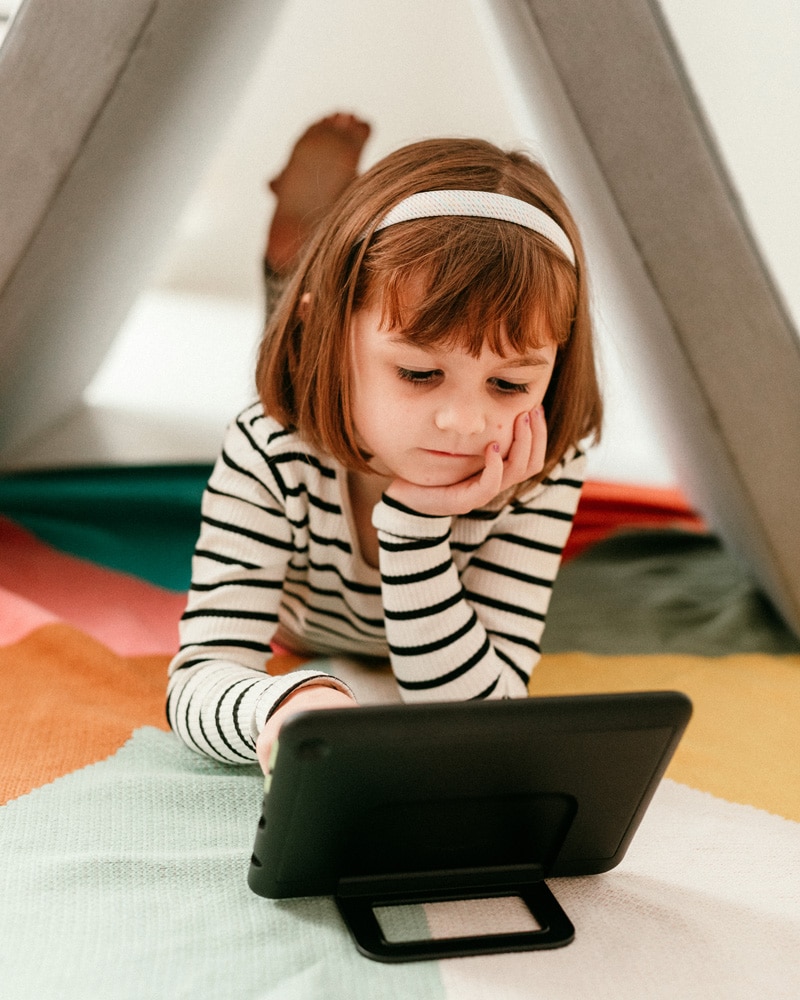 A girl laying on the ground playing with an Amazon Fire Kids Pro Tablet