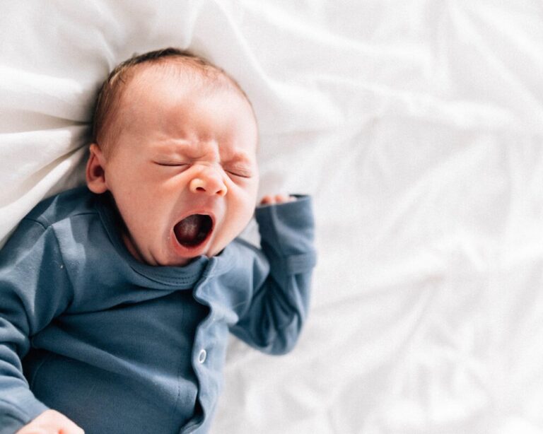 A yawning baby in a blue sleeper